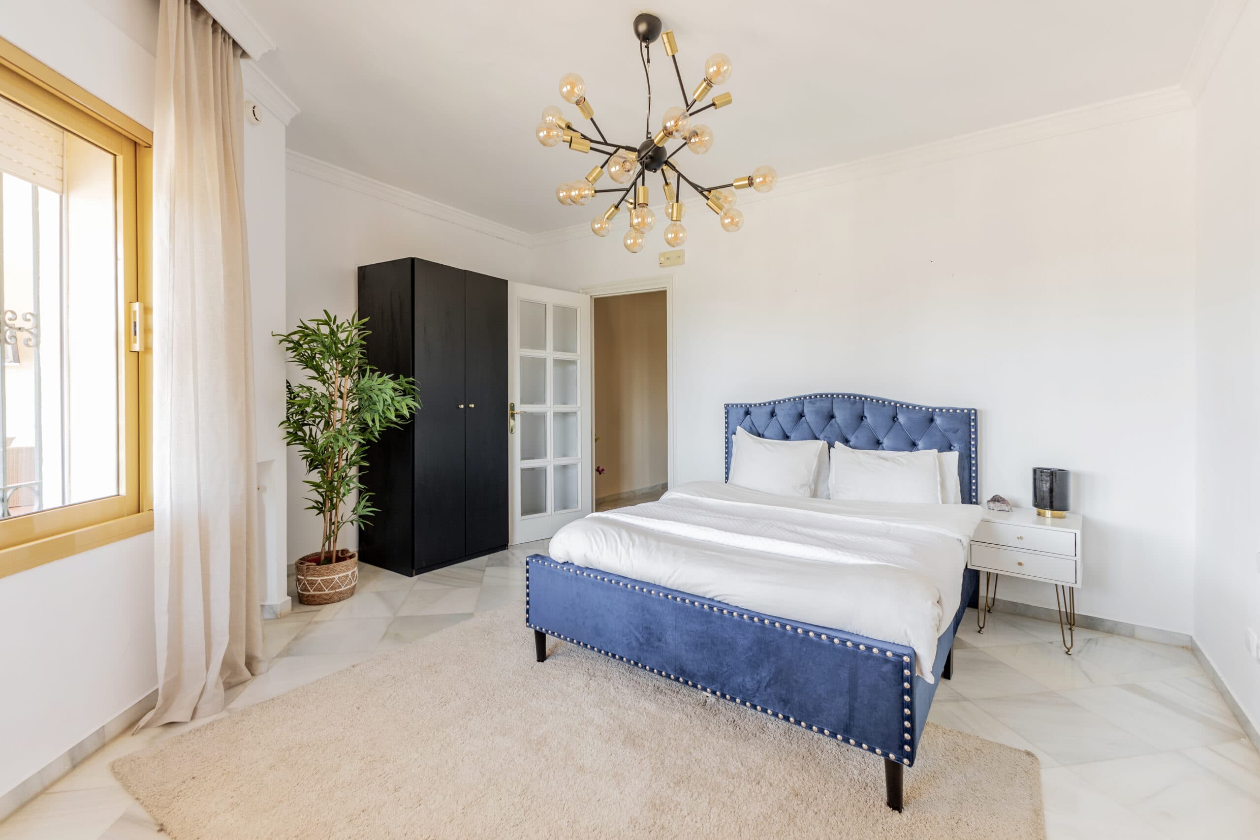 A private bedroom with a blue upholstered bed, marble floor and a brass chandelier